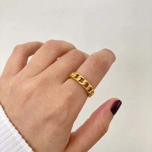Close-up of golden Cuban link chain ring worn on finger featuring woven metal texture
