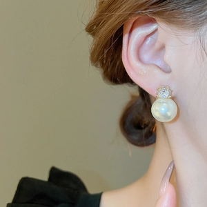 Gros plan d'une boucle d'oreille en grosse perle blanche avec zircon brillant sur l'oreille