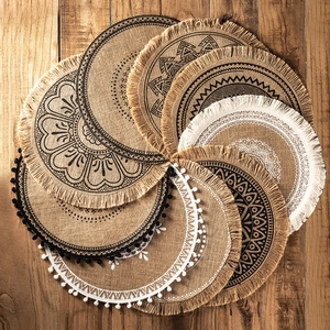 Handwoven round jute placemats with mandala patterns and fringe on wooden background