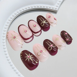 Pink and burgundy press-on nails with starburst bow designs and sparkling rhinestones