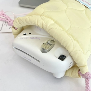 Detailed close-up of a pale yellow quilted cotton drawstring bag holding a compact camera