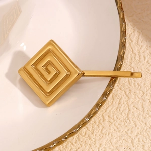 Vue rapprochée d'une barrette géométrique dorée avec motif grec sur plat en céramique