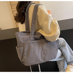 Détail d'un sac cabas en velours côtelé gris avec poche latérale porté par un mannequin