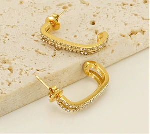 Detail view of U-shaped gold earrings with paved cubic zirconia on beige stone base