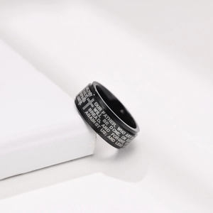 Detail of black spinning ring featuring engraved cross and scripture on white background