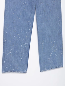 Détail du pantalon en jean bleu avec des strass argentés brillants sur fond blanc