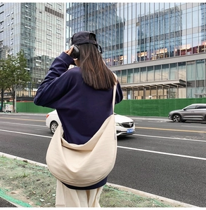 Detail of a large off-white crescent oxford bag shown on model in a city street