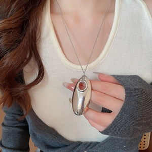 Close-up of a large silver oval mirror metal pendant necklace worn by a model over beige knitwear