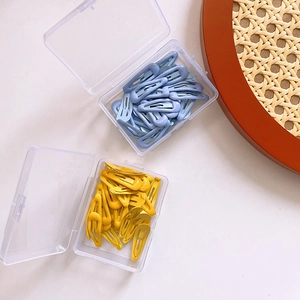 Macro view of light blue and yellow teardrop hair clips in transparent storage boxes