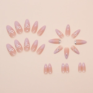 Macro view of almond press-on nails with pink gradient, white bows, and tiny rhinestones