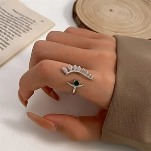 Detail of silver evil eye open ring with green stone on vintage book background