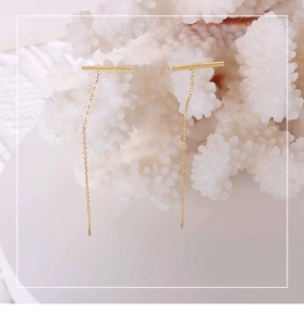 Detail view of 18k gold linear bar drop earrings displayed on a white coral stand