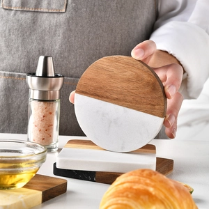 Hand picking up a marble and acacia wood coaster from a set of round and square mats