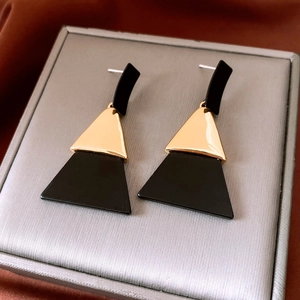 Close-up of geometric black and gold acrylic triangle drop earrings on a soft jewelry box