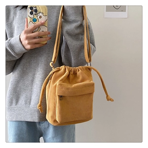 Detail of yellow corduroy bucket bag showing drawstring closure and front zipper pocket