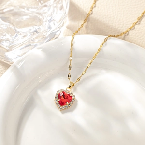 Macro shot of gold heart pendant necklace with red zircon stone on white ceramic