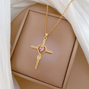 Detailed shot of gold cross and pink heart gemstone pendant on beige jewelry box