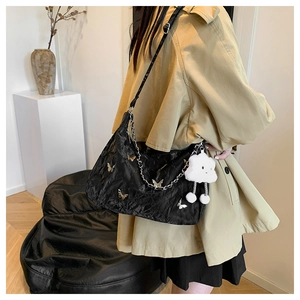 Detail of black pleated shoulder bag with gold butterfly accent and white plush charm