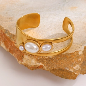 Detail of gold open cuff bracelet with three pearls on a natural stone background