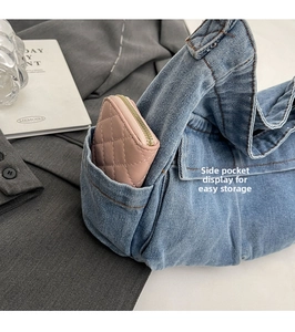 Detail view of denim tote side pocket showing storage of a pink wallet with brown stitching