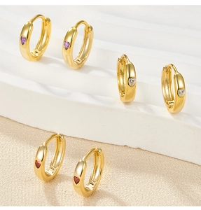 Detail of three pairs of gold-plated heart-shaped diamond earrings in red, white, and purple