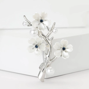 Detail of silver plum blossom brooch with pearls and blue gemstones on white background