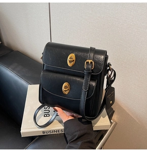 Detail view of black faux leather crossbody bag with golden oval twist locks and logo tag