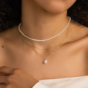 Close-up of triple-layered gold necklace with pearls and water drop pendant on neck