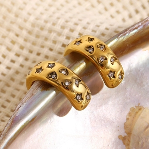 Macro shot of gold-plated star and heart-shaped earrings with clear zircon stones