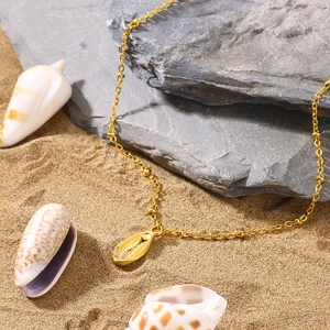 Detail of gold seashell necklace with small beads on a beach with shells and rocks