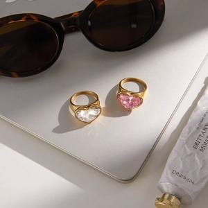 Elegant gold heart rings with clear and pink crystals on a lifestyle background