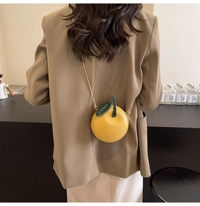 Detail of cute yellow apple-shaped crossbody bag with gold chain and leaf decoration