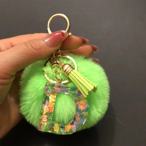 Close-up of green pompom keychain with resin letter D and colorful heart sequins