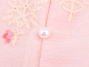 Detail van de roze geborduurde jurk met bloemenpatronen en een glanzende parelknoop