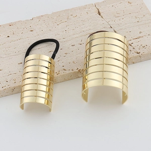 Detail view of a gold metallic curved hair cuff with a striped cutout design on stone