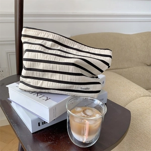 Chic black and white striped cosmetic bag on a wooden table with coffee and book