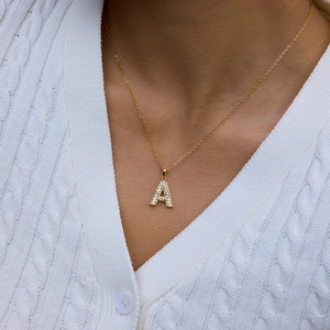 Elegante goldene Herzkette mit Buchstaben A und Strasssteinen auf weißem Strickpullover