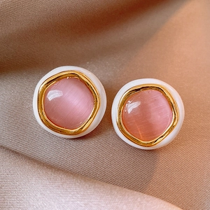 Detailed close-up of pink cat eye stud earrings with gold plating on champagne satin fabric