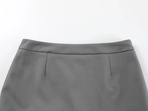 Detail view of grey mini skirt waistline showing woven texture and pleating craftsmanship