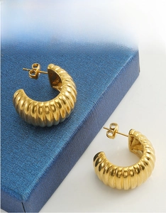 Gros plan de boucles d'oreilles dorées en C avec texture rayée sur boîte à bijoux bleue