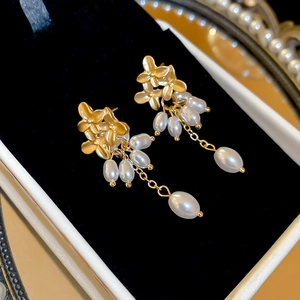 Detail of golden flower earrings with pearl tassels displayed on a black velvet box
