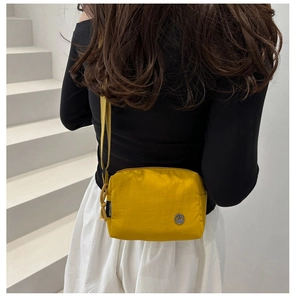 Detail of a bright yellow nylon shoulder bag with a metal logo and woven strap