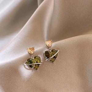 Detailed macro view of green and amber heart zircon stud earrings on champagne silk fabric
