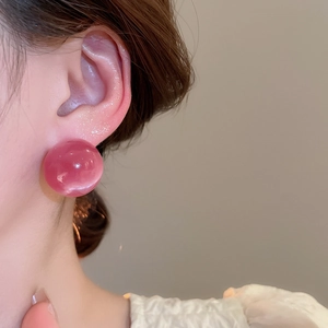 Close-up of a pink resin ball stud earring worn on the ear showing glossy finish