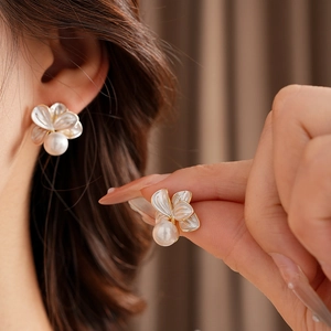 Gros plan d'élégantes boucles d'oreilles fleurs dorées avec perle et nacre blanche