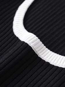 Close-up of ribbed knit texture on a black round neck sweater with white contrast piping