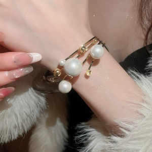 Detailed close-up of multi-layer gold cuff bracelet with elegant white pearls on wrist