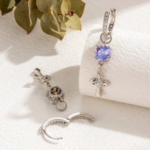 Silver hoop earrings with purple gemstone and fleur-de-lis cross pendant in a soft still life