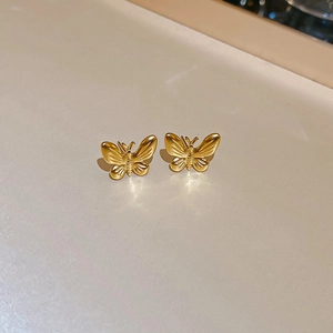 Macro shot of gold butterfly stud earrings with detailed wings on a minimalist beige surface