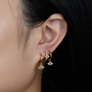 Detail shot of three golden evil eye earrings with blue crystals worn by a model